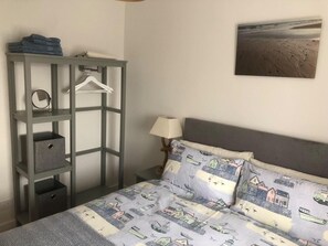 Ein Schlafzimmer mit einem Bett, einem Nachttisch, einer Wandlampe, einem gerahmten Bild und einem grauen Kleiderschrank mit Regalen.