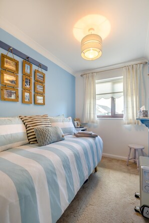 A bedroom with a bed, a bedside table, a window with curtains, and wall-mounted picture frames. - 2 Bed in Walcott (oc-c46378) (Walcott)