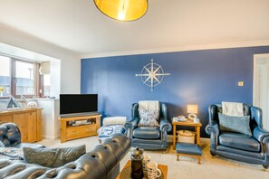 Ein Wohnzimmer mit Fernseher, Ledersofas, einem Couchtisch und einem an der Wand befestigten Kompass.