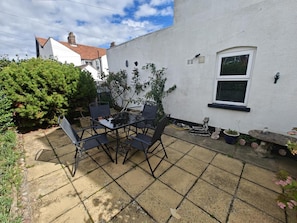 A patio with a table and chairs, a small garden, and a white building with a window. - 2 Bed in Overstrand (oc-s46412) (Overstrand)