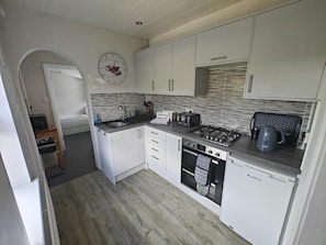 A compact kitchen with white cabinets, a built-in oven, a gas stove, and a coffee machine. - 2 Bed in Overstrand (oc-s46412) (Overstrand)