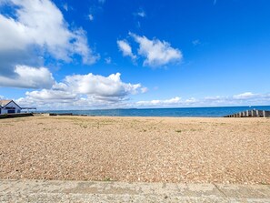 Ein Kiesstrand bei klar blauem Himmel und weiter Meerblick.