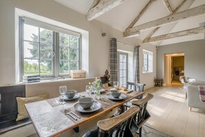 A dining area with a long table set for four, large windows, and a view of greenery outside. - 2 Bed in Northrepps (oc-c46373) (Northrepps)