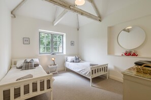 Een slaapkamer met twee eenpersoonsbedden, een raam, een nachtkastje met een lamp, een spiegel en een klein plankje met decoratieve objecten.