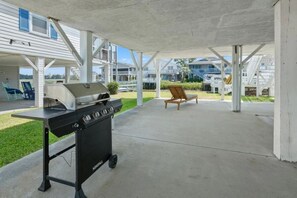 Une terrasse extérieure équipée d’un barbecue, de chaises et d’un espace abrité offrant une vue sur les bâtiments.