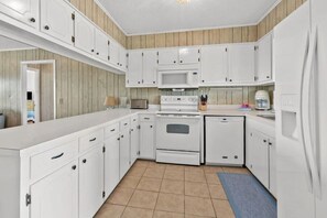 Une cuisine de taille réduite avec des meubles blancs, un four à micro-ondes, une cuisinière et un lave-vaisselle.