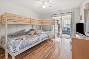 A bunk bed with a patterned bedspread, a ceiling fan, and a television on a wooden cabinet. - Beautiful Cherry Grove Beach House (North Myrtle Beach)