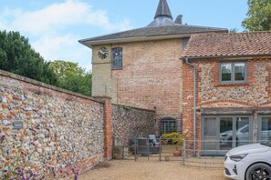 A stone wall with a clock tower, a car parked in front, and a gravel driveway. - 3 Bed in Letheringsett (oc-m46374) (Letheringsett)