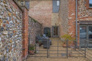 Une cour intérieure avec un mur en pierre, un portail en métal et un espace aménagé avec des chaises et une table.