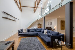 Un salon moderne avec un canapé d’angle, une table basse et un escalier menant à un niveau supérieur.