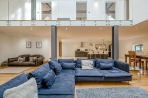 A modern living room with a sectional sofa, a dining area, and a kitchen in the background. - 3 Bed in Letheringsett (oc-m46374) (Letheringsett)