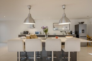 A modern kitchen with a central island, pendant lighting, and a dining area with four chairs. - 3 Bed in Letheringsett (oc-m46374) (Letheringsett)