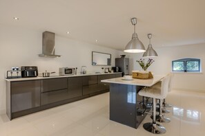 Une cuisine moderne dotée d’un îlot central, d’appareils électroménagers en acier inoxydable et de luminaires suspendus.