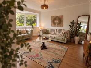 Un salon avec un canapé, une table basse et un grand miroir. On y trouve également des plantes et une fenêtre donnant sur un paysage verdoyant.