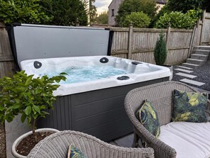 Ein Whirlpool mit Holzterrasse, umgeben von Korbmöbeln und einem Blumentopf.