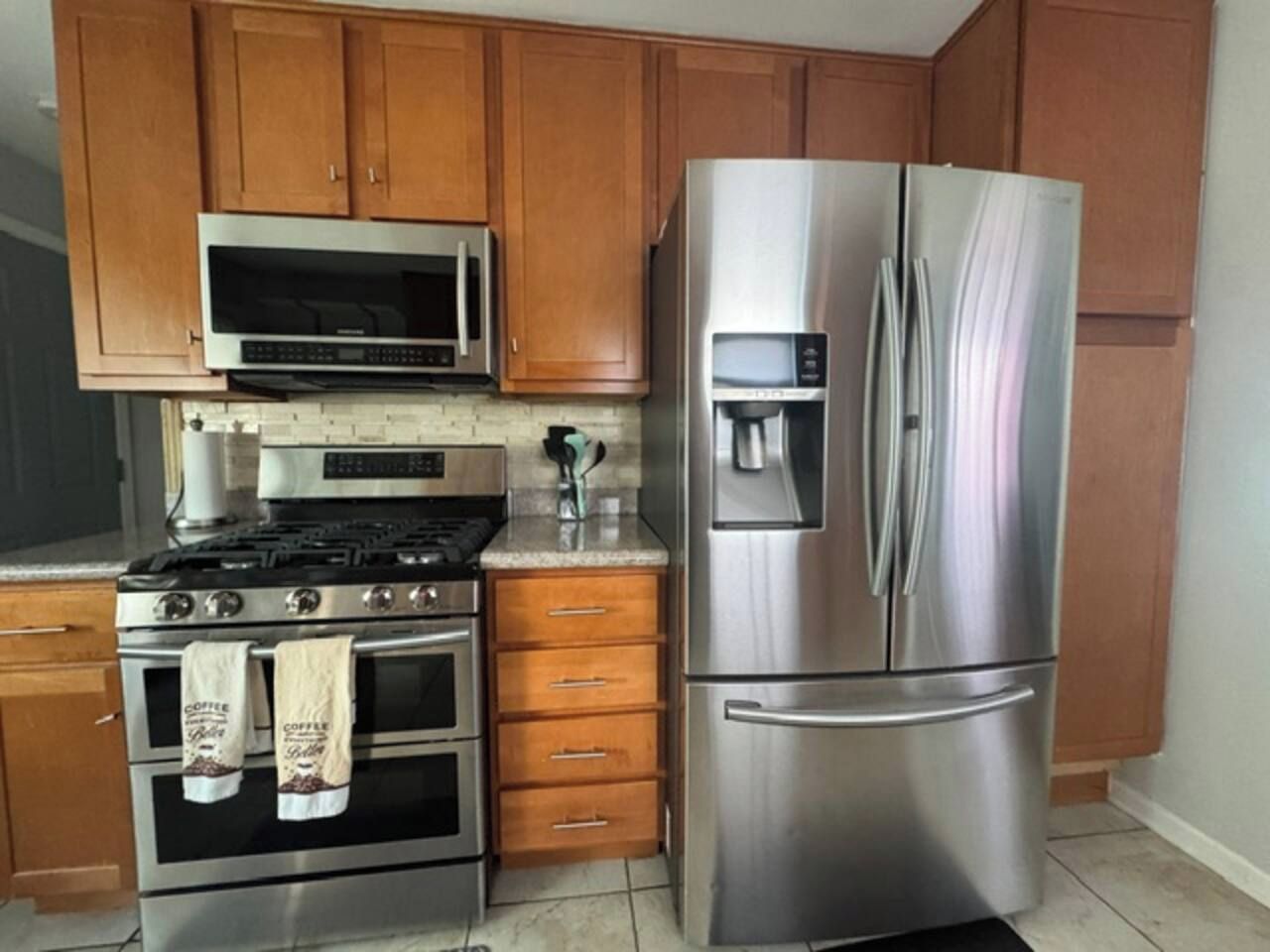 A kitchen with wooden cabinets, a stainless steel refrigerator, a microwave, a stove, and a coffee maker.