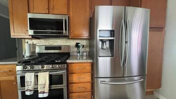 A kitchen with wooden cabinets, a stainless steel refrigerator, a microwave, a stove, and a coffee maker.
