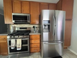 A kitchen with wooden cabinets, a stainless steel refrigerator, a microwave, a stove, and a coffee maker. - Cozy Lakeview Home Minutes from O'Hare (Des Plaines)