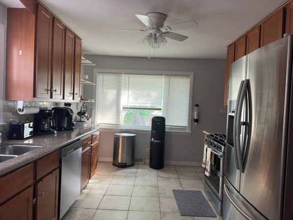 A kitchen with wooden cabinets, a stainless steel refrigerator, a stove, and a ceiling fan. - Cozy Lakeview Home Minutes from O'Hare (Des Plaines)