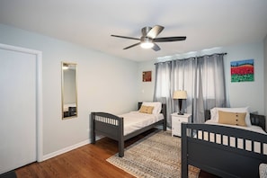 A bedroom with two single beds, a ceiling fan, a bedside table with a lamp, a mirror, and a painting on the wall. - Cozy Lakeview Home Minutes from O'Hare (Des Plaines)