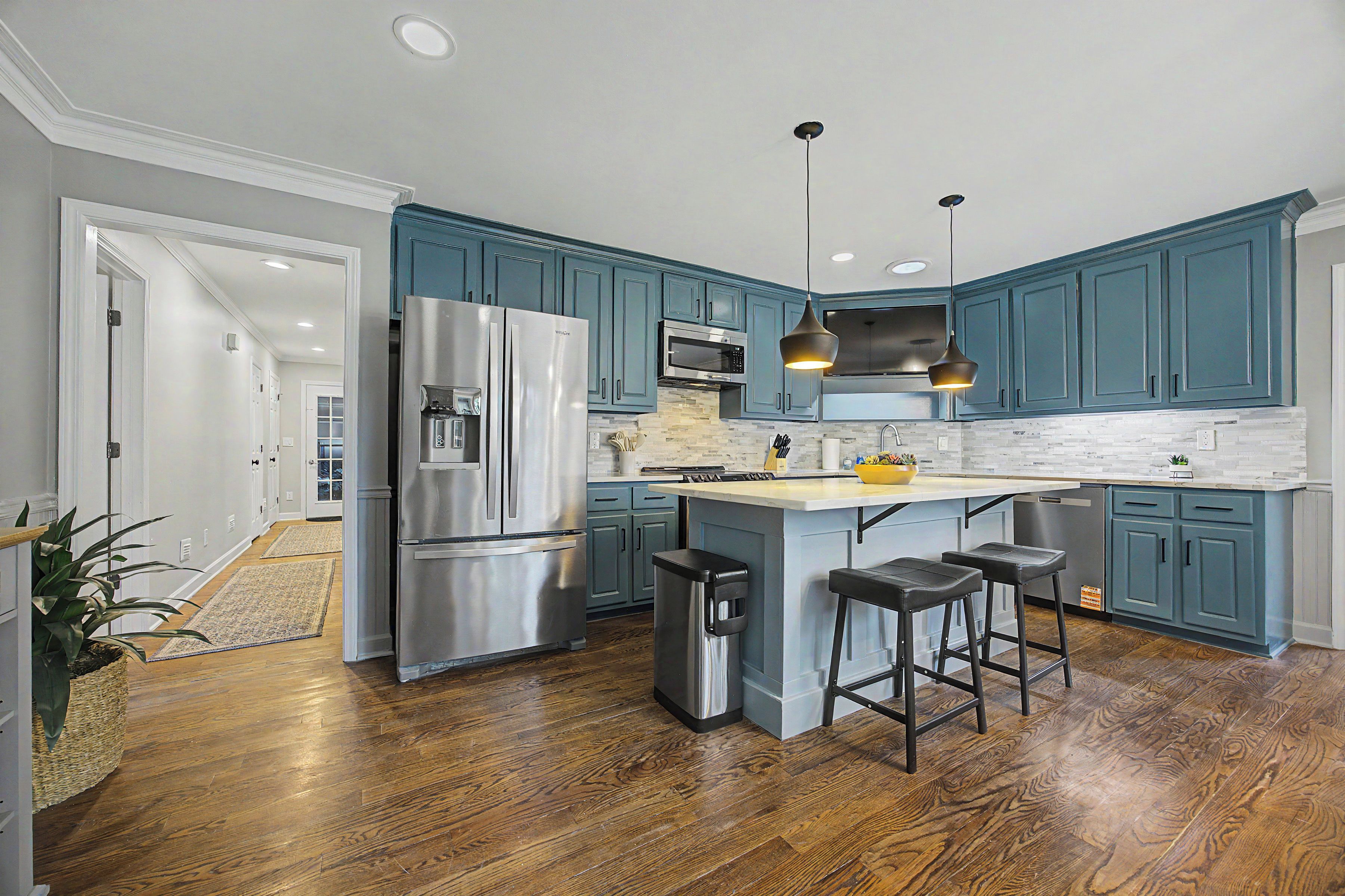 A modern kitchen with a central island, stainless steel appliances, and teal cabinetry.