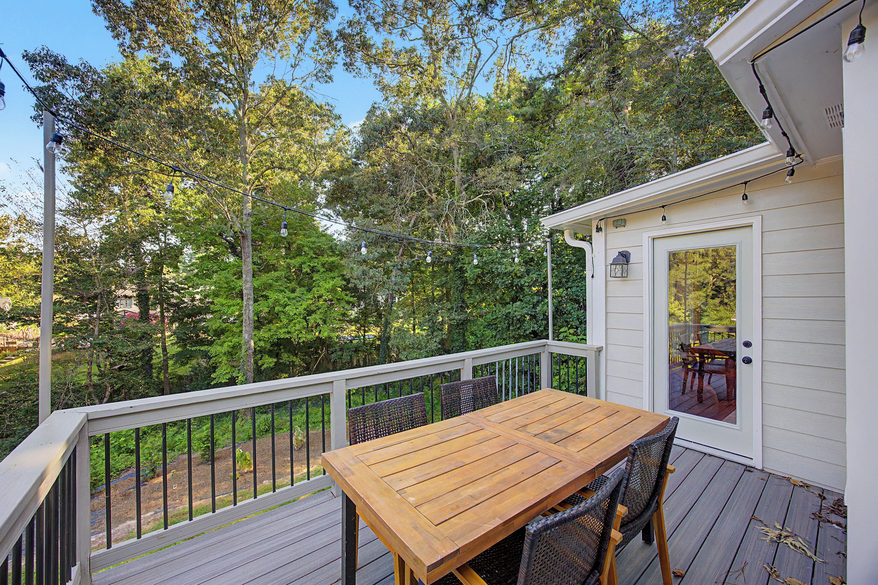 A wooden deck with a table and chairs, surrounded by a white railing, overlooking a lush green landscape.