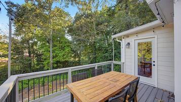 A wooden deck with a table and chairs, surrounded by a white railing, overlooking a lush green landscape.