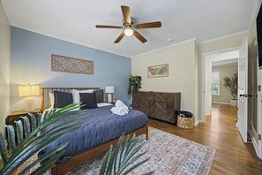 A bedroom with a bed, a ceiling fan, a nightstand, a lamp, a decorative wall piece, a potted plant, and a door leading to another room. - Spacious 4BR Buford Home Near Mall of Georgia (Buford)
