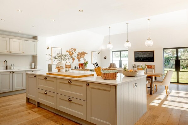 A modern kitchen with a large island, wooden flooring, and pendant lighting. - 4 Bed in Beccles (oc-v46416) (Beccles)