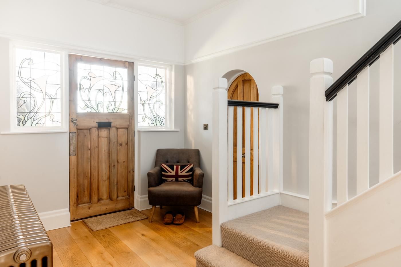 A staircase with a wooden handrail, a chair with a Union Jack cushion, and a wooden door with a glass window.