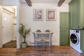 A compact kitchen with a washing machine, a dining table with chairs, and two framed botanical prints on the wall. - 1 Bed in Haworth (oc-b46415) (Haworth)