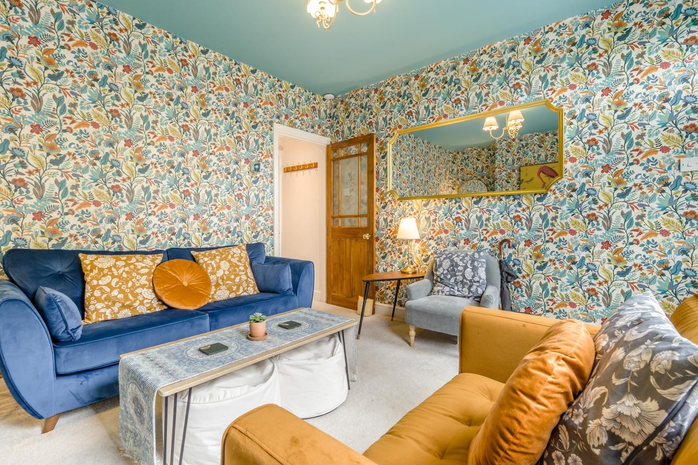 A living room with a blue sofa, a coffee table, and a patterned wallpaper.