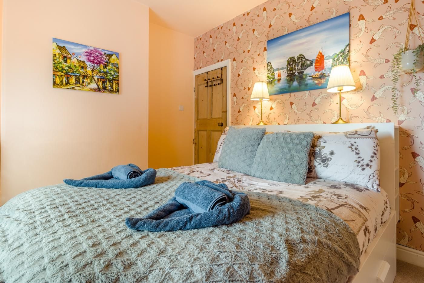 A hotel room with a bed, two towels, a painting, a lamp, and a door.