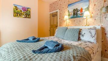A hotel room with a bed, two towels, a painting, a lamp, and a door.