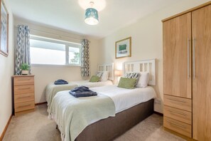 A bedroom with two beds, a wardrobe, a desk, and a window with curtains. - 3 Bed in Callington (oc-t46349) (Harrowbarrow)