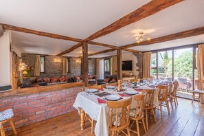 Uma sala de jantar com parede de tijolos, vigas de madeira e uma mesa comprida posta para refeição.