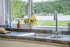 A kitchen with a granite countertop, a sink, and a window with a view of a hedge. - 3 Bed in Groesffordd (oc-g46338) (Groesffordd)