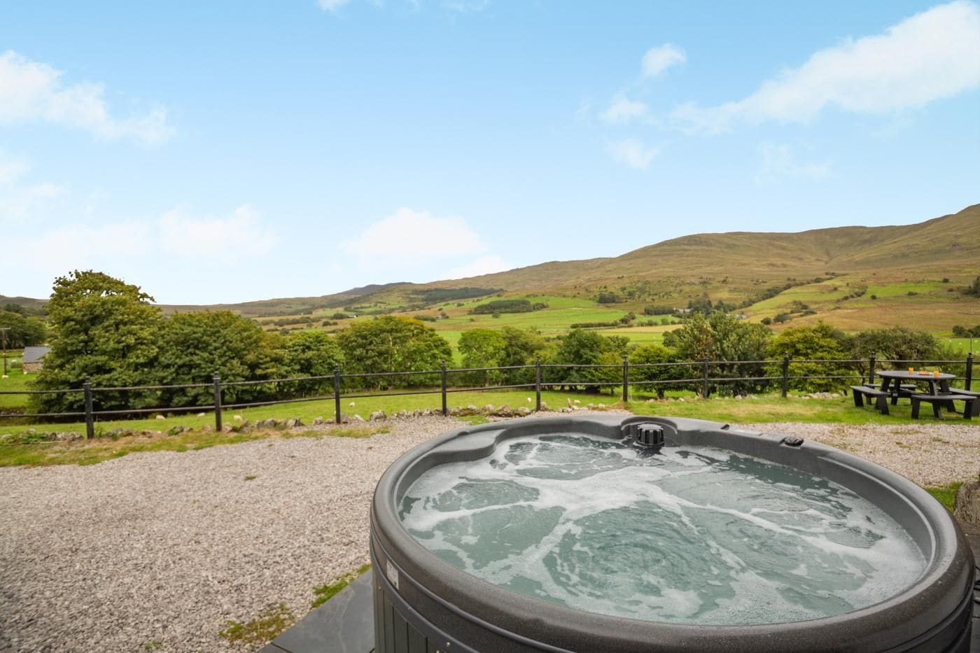 Jacuzzi con vista a un paisaje rural, que incluye colinas y un área cercada con mesas de picnic.