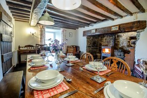 A dining area with a wooden table set for a meal, a stone fireplace, and exposed wooden beams on the ceiling. - 4 Bed in Dolgellau (oc-g46068) (Brithdir and Llanfachreth)