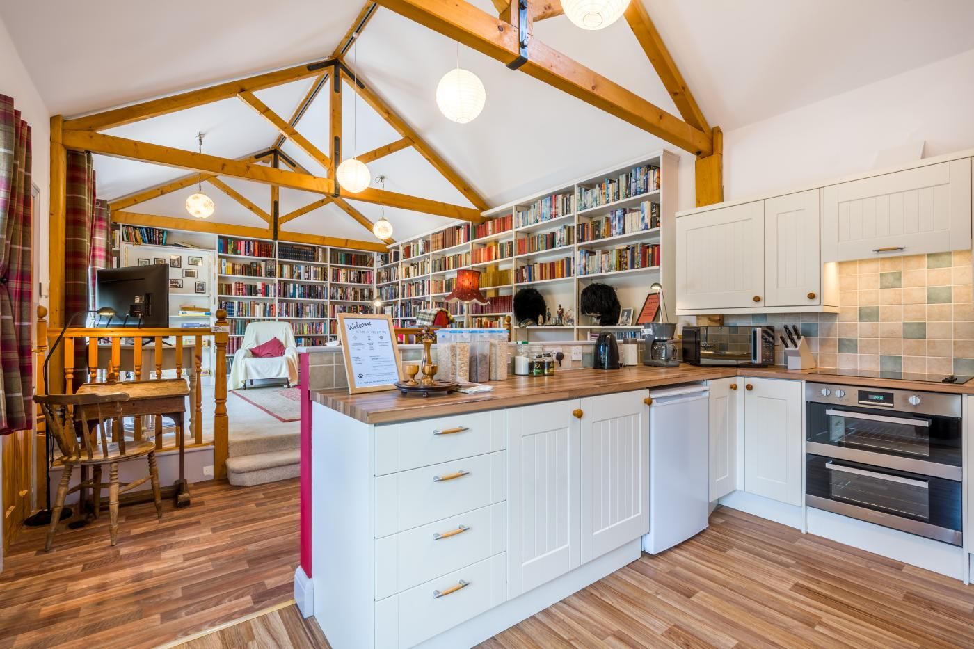 A spacious kitchen with wooden beams, a central island with a sink, and a built-in bookshelf filled with books.