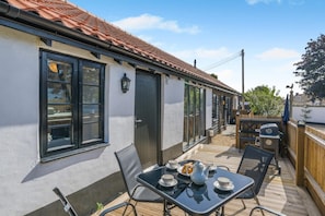 A patio with a table set for tea, a barbecue grill, and a wooden fence. - 2 Bed in Lakenheath (oc-t46347) (Lakenheath)