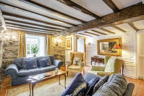A rustic interior with exposed wooden beams, stone walls, and a variety of seating including a sofa, armchairs, and a patterned ottoman. - 5 Bed in Betws Garmon (oc-bibd) (Betws Garmon)
