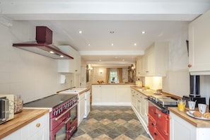 A modern kitchen with a central island, built-in oven, and a red range hood. - 5 Bed in Betws Garmon (oc-bibd) (Betws Garmon)