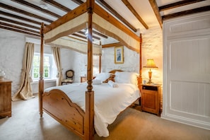 Ein Bett mit Baldachin, ein Holzbettgestell, ein Nachttisch mit Lampe und ein Fenster mit Vorhängen.