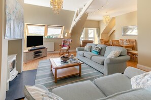 A spacious living room with a television, sofa, and dining area. - 3 Bed in Fowey (oc-h46394) (Fowey)