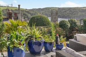A terrace with potted plants, a bird, and a view of a castle and water. - 3 Bed in Fowey (oc-h46394) (Fowey)