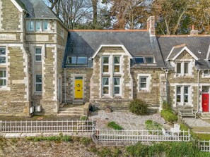 A stone building with multiple windows and a yellow door, surrounded by a white fence. - 3 Bed in Fowey (oc-h46394) (Fowey)