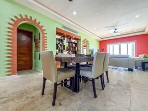 A dining area with a table and chairs, a bookshelf, and a red wall. - Isla 33 Two Bedroom Villa | Poolside & Caribbean Views (Isla Mujeres)