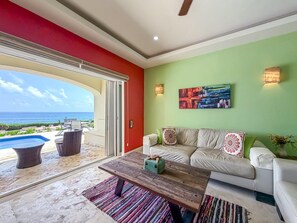 A living room with a sofa, coffee table, and a view of the ocean. - Isla 33 Two Bedroom Villa | Poolside & Caribbean Views (Isla Mujeres)