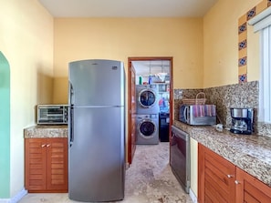 A compact kitchen with a refrigerator, washing machine, and a toaster. - Isla 33 Two Bedroom Villa | Poolside & Caribbean Views (Isla Mujeres)